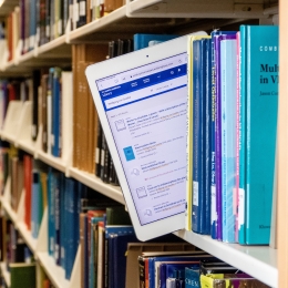 An iPad being pulled from a shelf of print books 