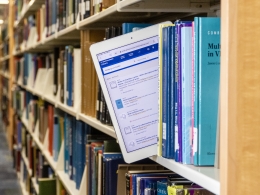 A person pulling an ipad from a bookshelf.