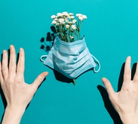 Two hands arranging flowers inside a surgical mask