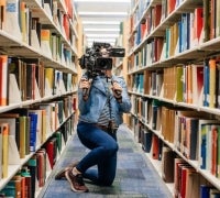 woman holding video camera behind stacks