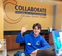 Student assistant waving at Collaborate Helpdesk in Library