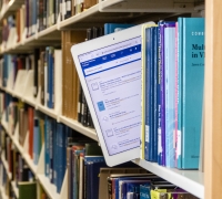 A person pulling an ipad from a bookshelf.