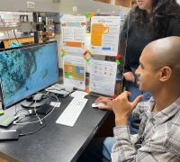 Caves Lab PhD student Bryce Barbee and research technician Miya Ball observe the behavior of cleaner shrimp on a typical video brought back from their field site in Curaçao.